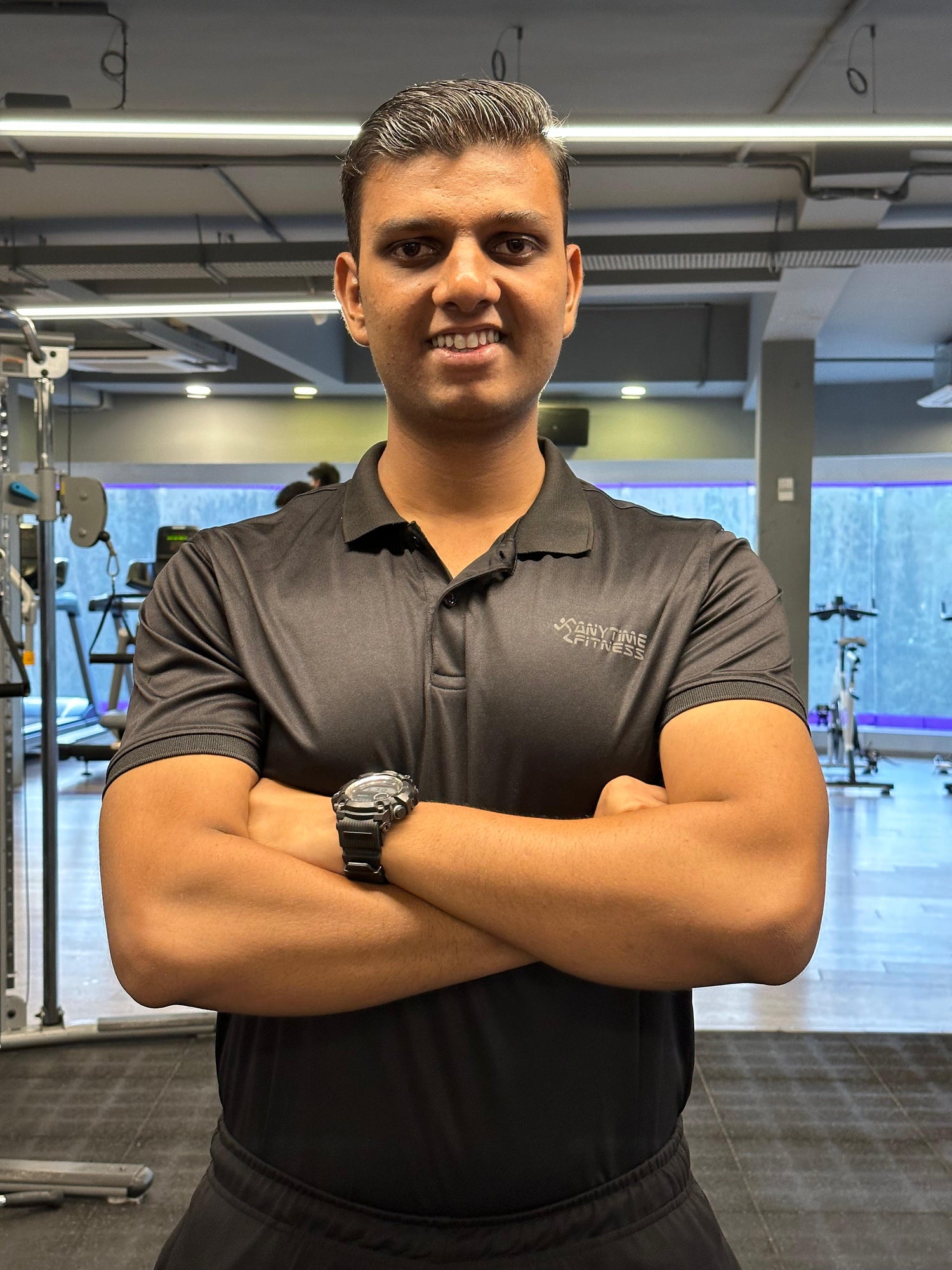 Man in a gym wearing a branded shirt with arms crossed